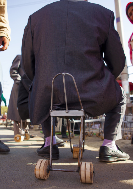 Uyghur Man Sitting On A Chair With Wheels Used To Harvest Cotton, Serik Buya Market, Yarkand, Xinjiang Uyghur Autonomous Region, China