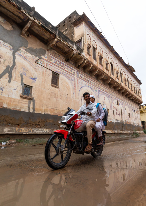 Indian people riding a motorbike and passing by an old historic haveli, Rajasthan, Nawalgarh, India