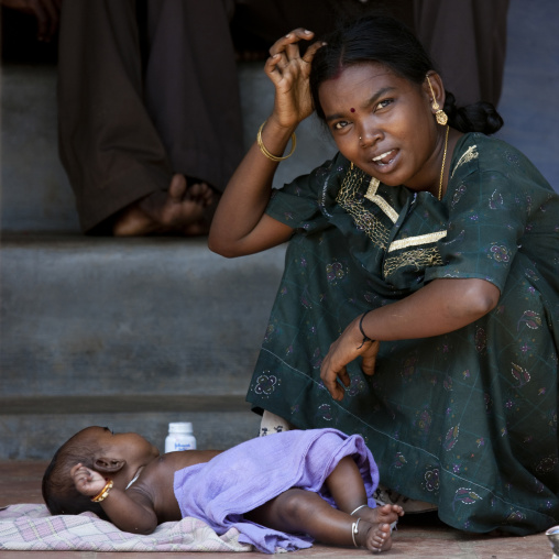 Squatting Mother Wearing Sari With Her Child Lying On A Blanket On The Floor At The Bottom Of Some Steps, Kanadukathan Chettinad, India