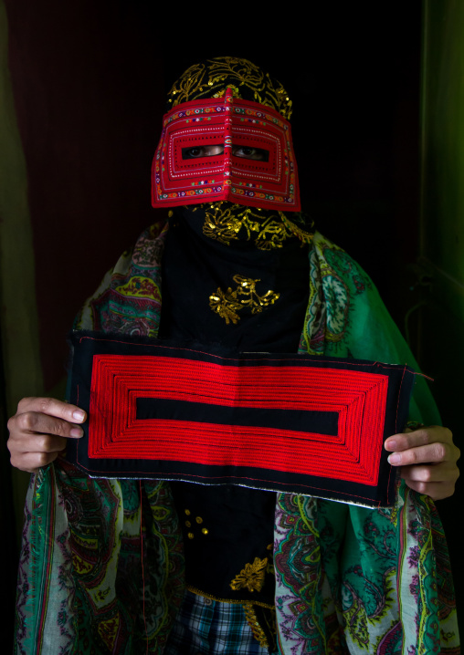 a bandari woman wearing a traditional mask called the burqa and showing one she is sewing, Hormozgan, Minab, Iran