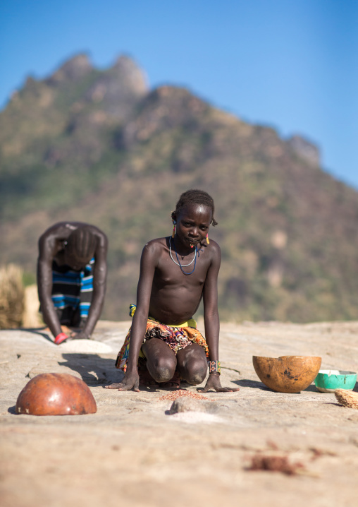 Larim tribe women grinding sorghum grains in holes in a rock, Boya Mountains, Imatong, South Sudan