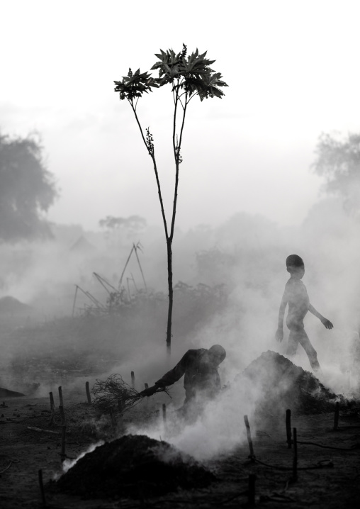 Mundari tribe boy taking care of the bonfires made with dried cow dungs to repel flies and mosquitoes, Central Equatoria, Terekeka, South Sudan