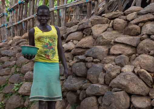 Lotuko tribe woman carrying food in front of a stone wall, Central Equatoria, Illeu, South Sudan